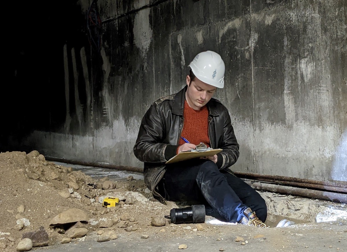 Daniel wearing hard hat seated in tunnel taking notes