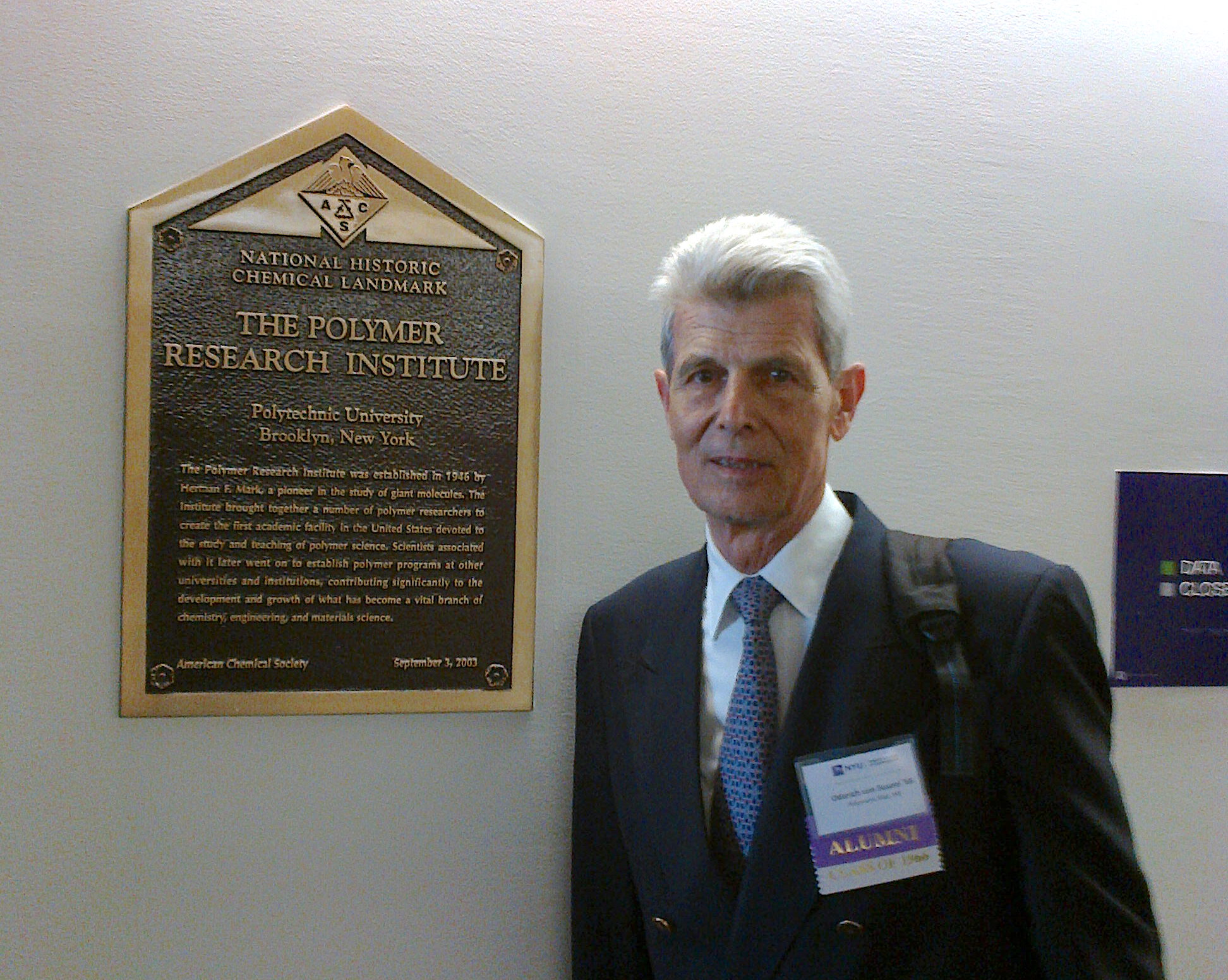 Alum Von susani standing next to commemorative plaque